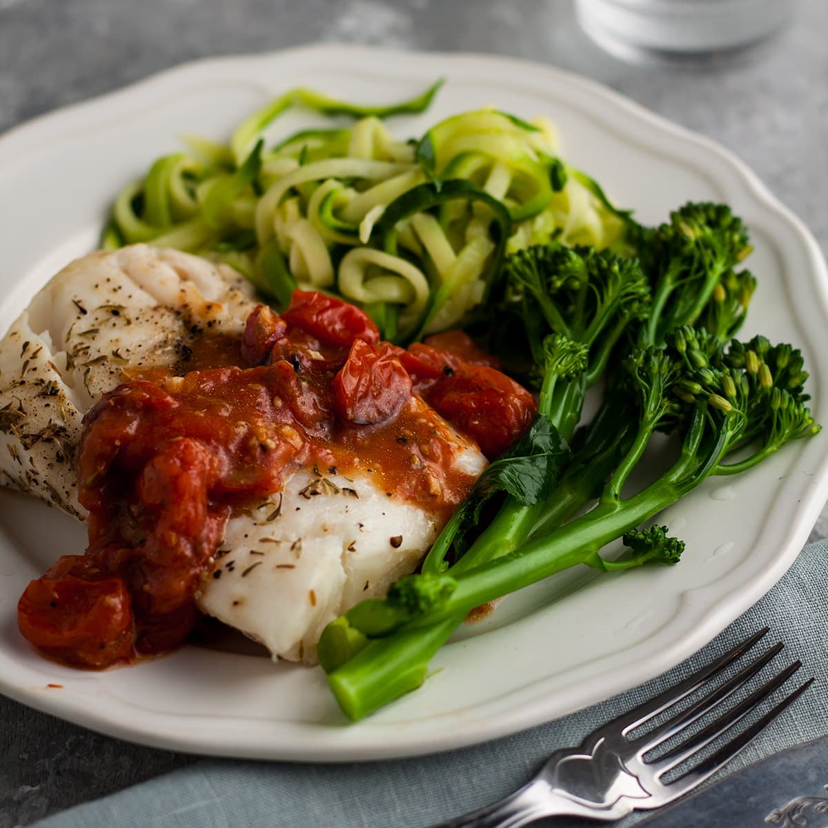 oven baked cod with chunky tomato sauce served on a plate with courgette and broccoli