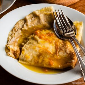 serving of crepe suzette with spoon and fork on a white plate.