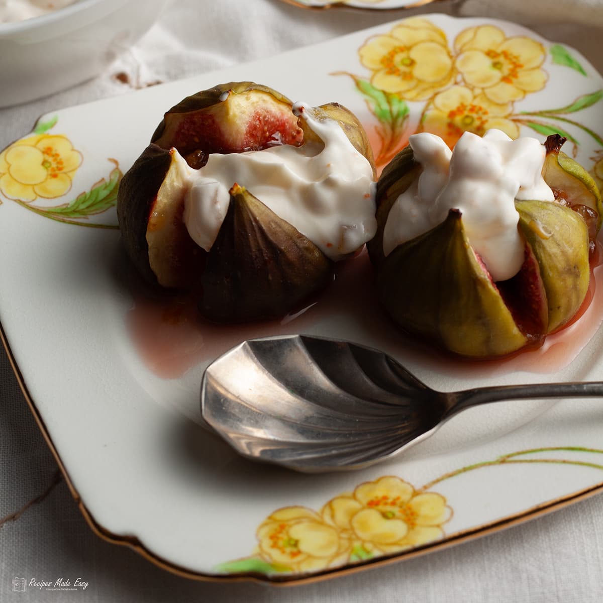 2 roasted figs topped with ginger and orange cream ion a dessert plate with a spoon.