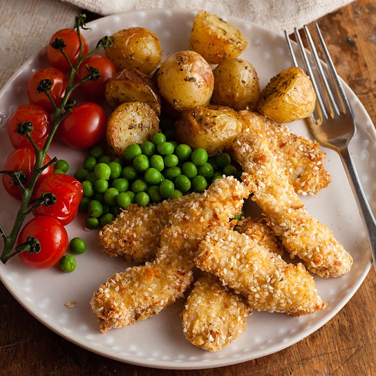 oven baked sesame chicken nuggets with roasted baby potatoes and peas on a plate.