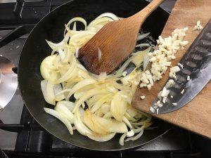 adding garlic to onions in pan