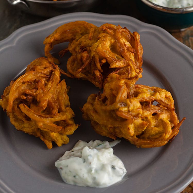 3 onion bhajis with cucumber raita on a serving plate