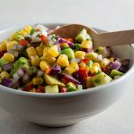 bowl of avocado and sweetcorn salsa with wooden spoon in bowl