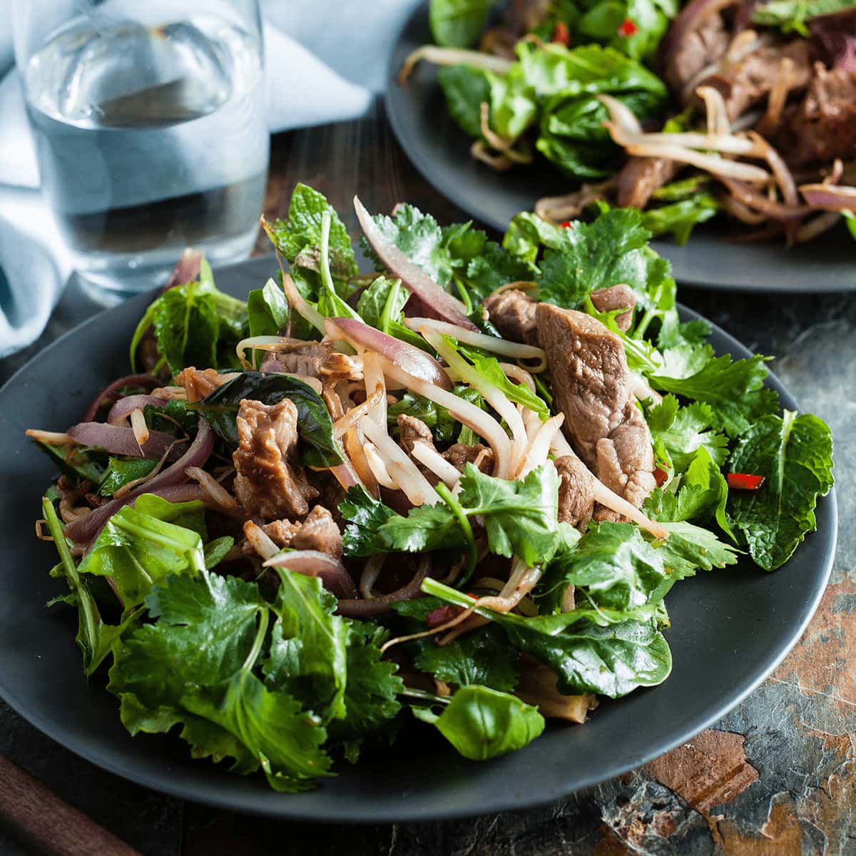 warm lamb salad with Thai dressing served with glass of water and napkin behind.