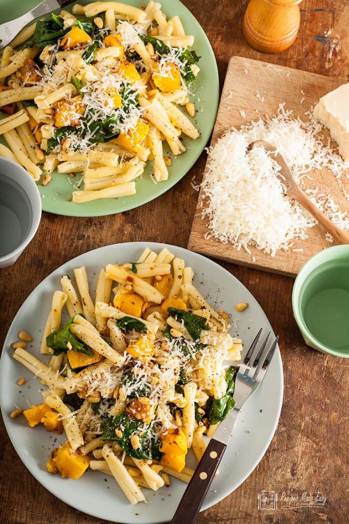 over head shot of two plates of pasta with roasted pumpkin and spinach .