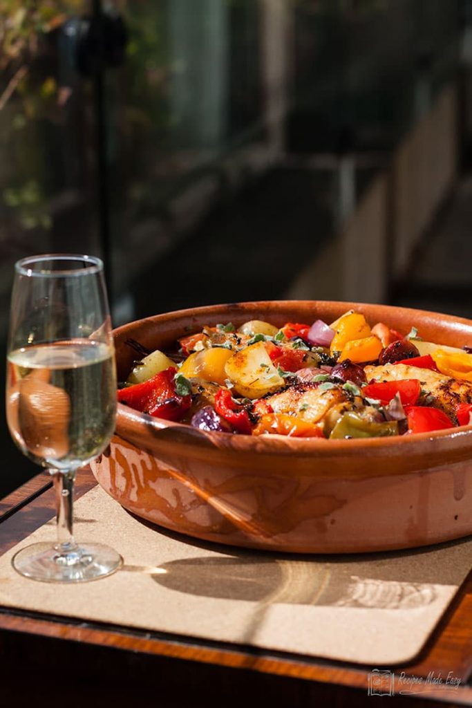 casserole dish with Spanish chicken and glass of wine on the side.