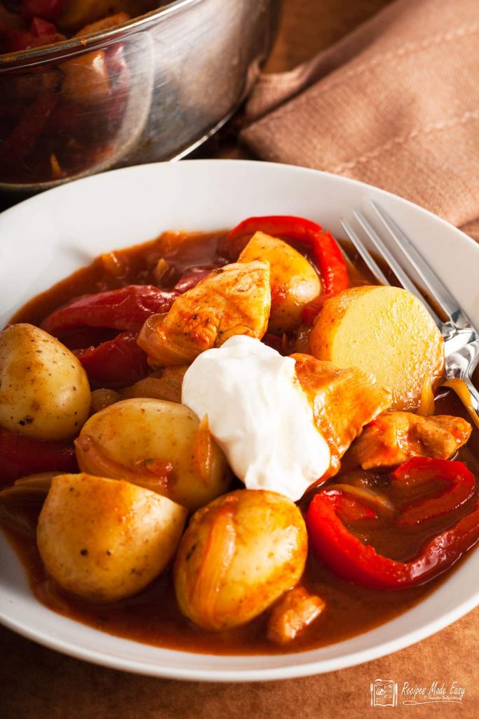 bowl of chicken and potato goulash with sour cream on top.