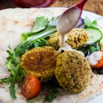 plate of baked falafel with bowl of salad and flat breads behind.