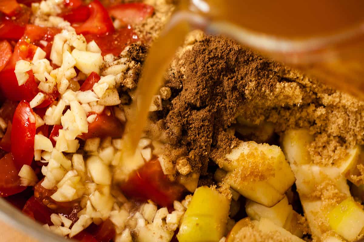 tomatao chutney ingredients in pan with vinegar being poured in.