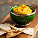 bowl of carrots with toasted flat breads on a wooden board.