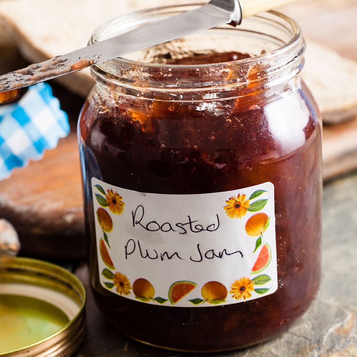 Open jar of roast plum jam with knife balanced on top.