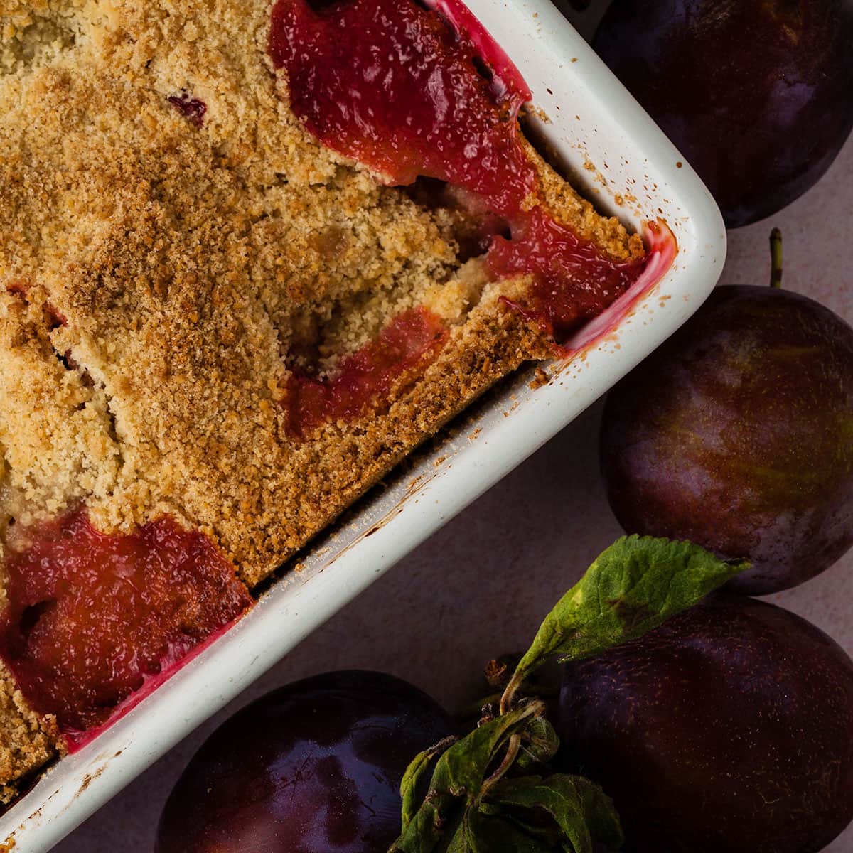 plum and pear crumble in baking dish surrounded by plums.