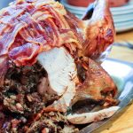 roast turkey on a carving tray with a slice removed showing the stuffing.