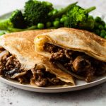 two beef and mushroom pancakes with green vegetable on a plate.