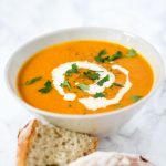 Bowl of carrot and coriander soup with bread on the side.