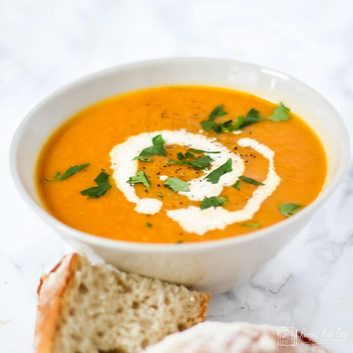 Bowl of carrot and coriander soup with bread on the side.