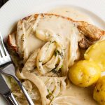 serving of pork with creamy fennel sauce served with new potatoes on a white plate with cutlery.