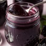 open jar of blackcurrant jelly with spoon ful of jelly on top. two jars behind.