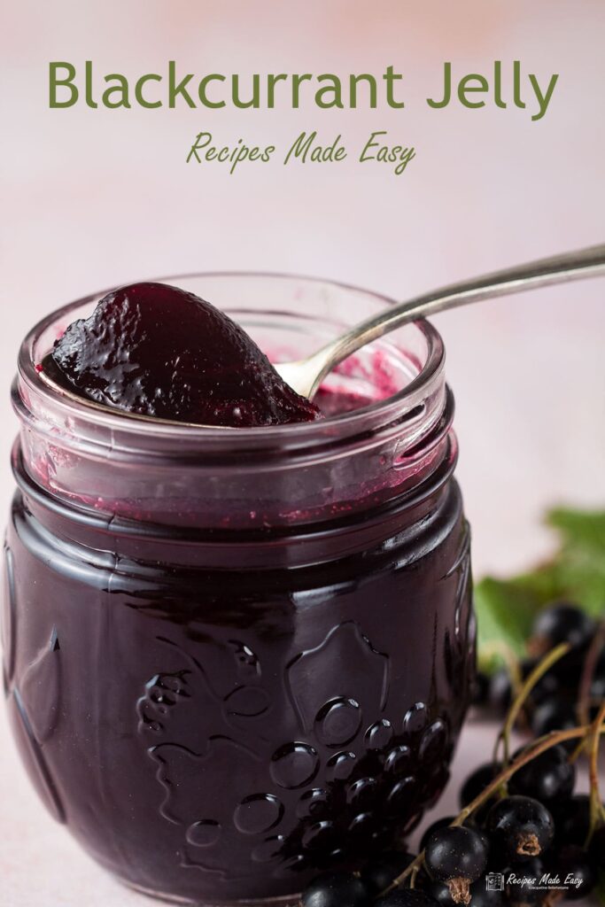 open jar of blackcurrant jelly with spoon. Fresh blackcurrants on the side.