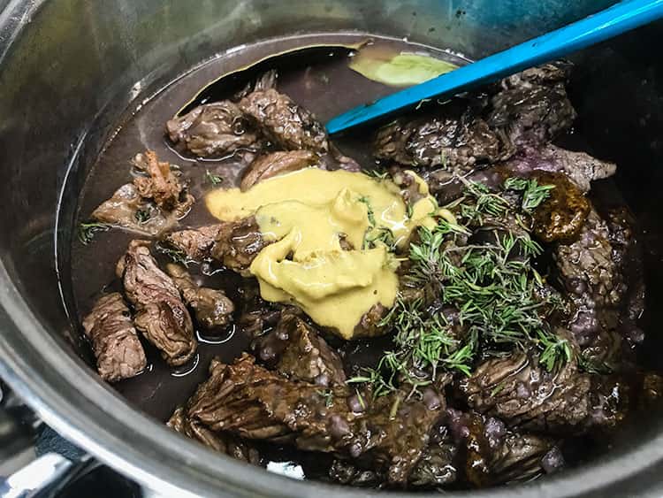 beef and lquid in saucepan with mustard and thyme added to pan.