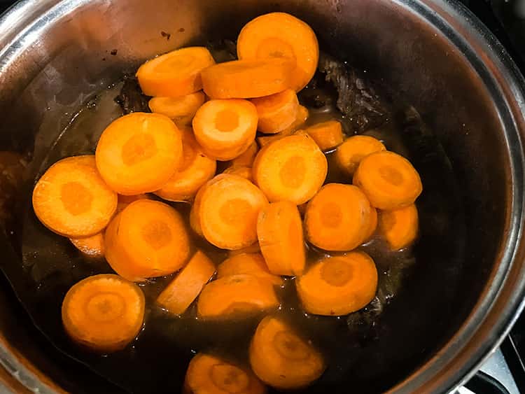 carrots added to cooked beef in saucepan.