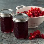 2 jars of redcurrant jelly with colander oof redcurrants behind.