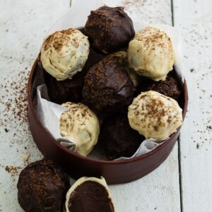 Coffee truffles coated in white and dark chcolate in a box. One broken open in front next to a whole truffle.