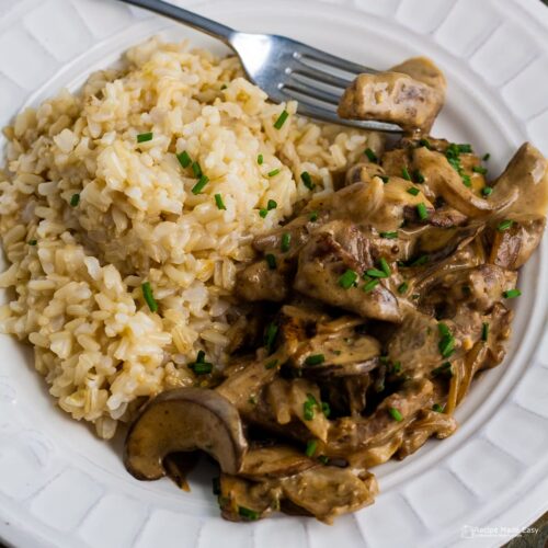 plate of easy beef stroganoff served with rice and garnished with snipped chives. Fork on the side of the plate.